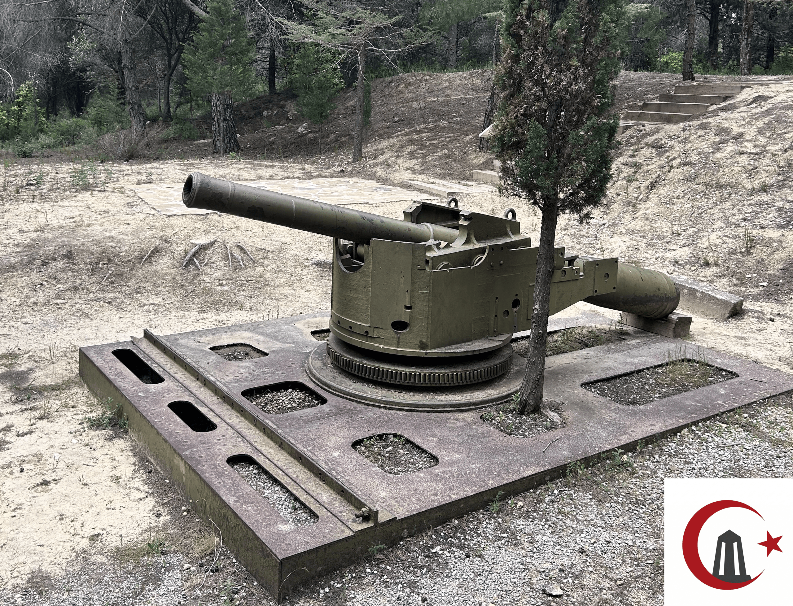 Çanakkale Şehitler Abidesi yolunda, çam ağaçları arasında metal kaide üzerinde duran yeşil renkli 15 cm'lik Krupp gemi topu.